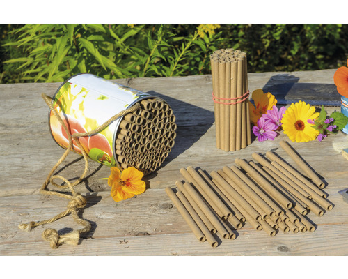 Insektenhotel mit Röhrchen und Blumen auf Holztisch