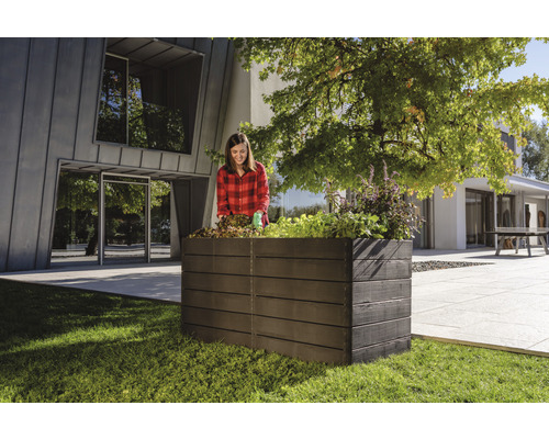 Frau bepflanzt ein Hochbeet im Garten vor einem modernen Haus.
