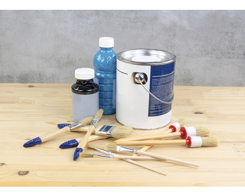 Seau de peinture, bouteilles de peinture et pinceaux sur une table en bois