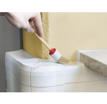 Une main applique de la peinture sur un mur avec un pinceau rond.