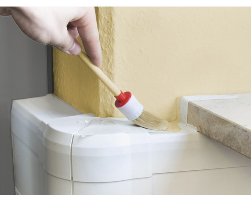 Une main applique de la peinture sur un mur avec un pinceau rond.