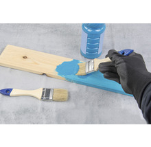 Une personne peint une planche de bois avec un pinceau et de la peinture.