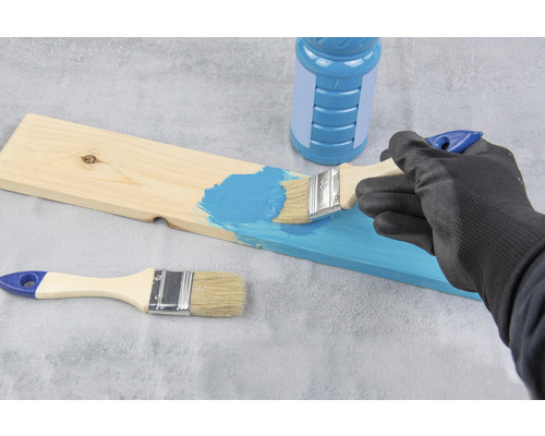 Une personne peint une planche de bois avec un pinceau et de la peinture.