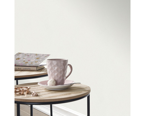 Detailaufnahme einer Wand mit Tapete neben einem Tisch mit Tasse und Buch