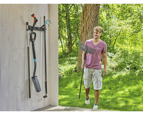 Outils de jardin sur un support mural avec un homme tenant un râteau