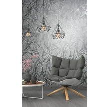 Salon avec fauteuil, table et suspensions géométriques devant un papier peint à motifs floraux