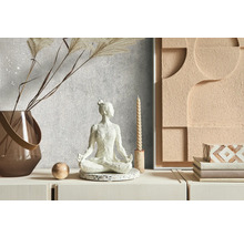 Dekorative Szene mit einer Meditationsfigur, einer Vase, einer Kerze und einem Wandbild auf einer Kommode.