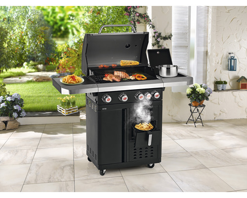 Grillszene im Freien mit Fleisch, Gemüse und Pommes Frites auf einem schwarzen Gasgrill mit vier Brennern.