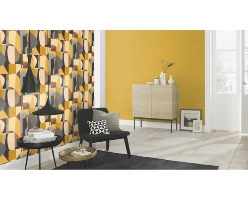 Wohnzimmer mit gemusterter Tapete, Kommode und Sessel.