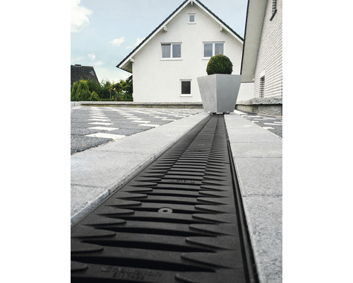 Caniveau de drainage en plastique dans une allée avec pavés et maison.