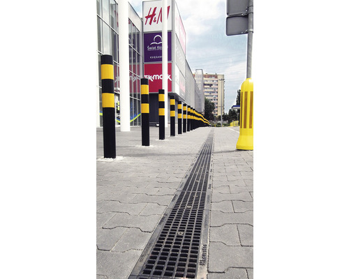 Extérieur avec caniveau de drainage et poteaux de barrage devant un centre commercial.