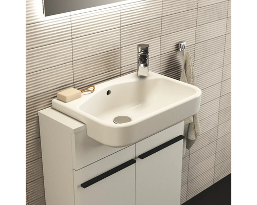 Waschtisch mit Unterschrank, Armatur, Seife und Handtuch vor einer Wand mit horizontalen Fliesen