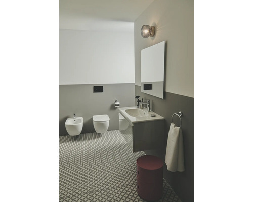 Badezimmer mit Bidet, Toilette, Waschbecken, Spiegel, Lampe und gemusterten Bodenfliesen