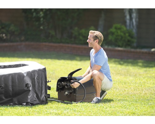 Ein Mann schliesst eine aufblasbare Whirlpool-Wanne an eine Pumpe an, um sie aufzublasen.