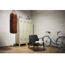 Szene mit Boxsack, Spind, Sessel, Fahrrad und Hanteln in einem Raum mit Backsteinmauer