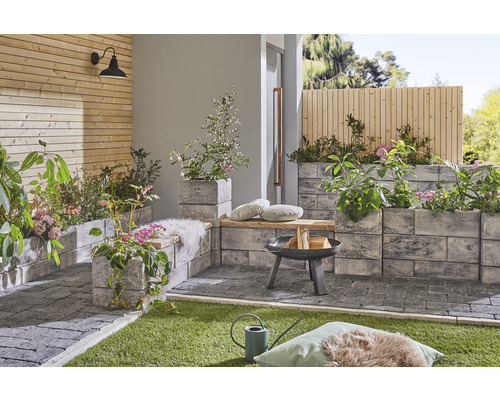 Espace extérieur aménagé avec pavés, foyer et bacs à plantes