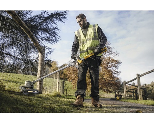Un homme utilise un coupe-bordure DeWalt dans un jardin près d''une clôture.