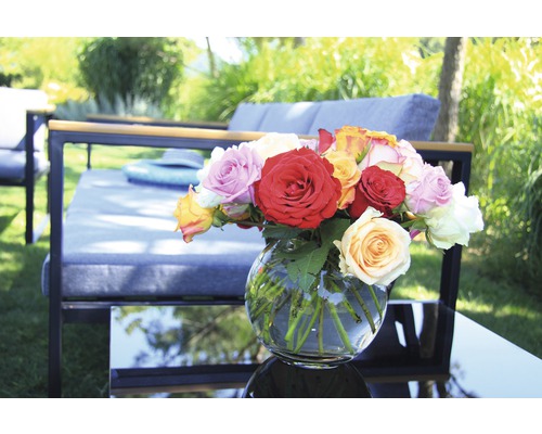 Un arrangement de roses dans un vase en verre sur une table de jardin avec des meubles de jardin en arrière-plan.
