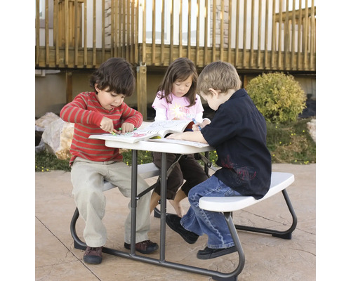 Kinder sitzen an einem Picknicktisch und malen in Büchern.
