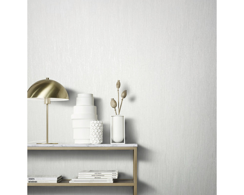 Nature morte décorative avec lampe de table, vases et livres devant un papier peint structuré