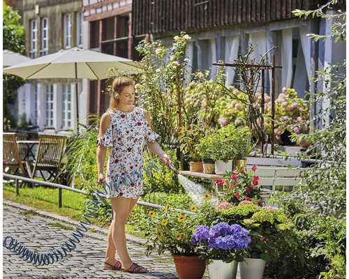 Frau giesst Blumen mit einem Gartenschlauch im Garten.