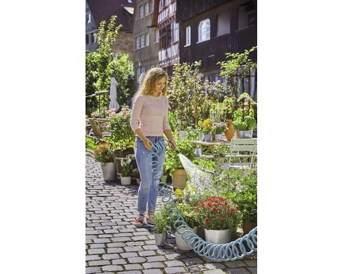 Frau giesst Blumen mit einem Gartenschlauch im Garten.