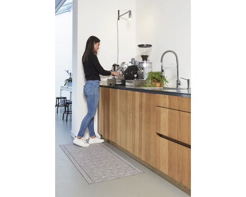 Femme préparant du café dans une cuisine lumineuse avec un tapis de cuisine