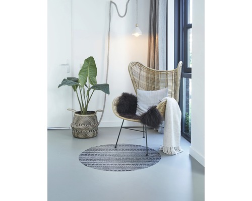 Helle Raumszene mit Korbsessel, Zimmerpflanze, rundem Teppich und Dekoration