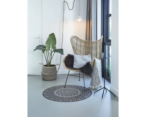 Wohnzimmer mit Rattan-Sessel, rundem Teppich mit Mandala-Muster und Zimmerpflanze im Korb
