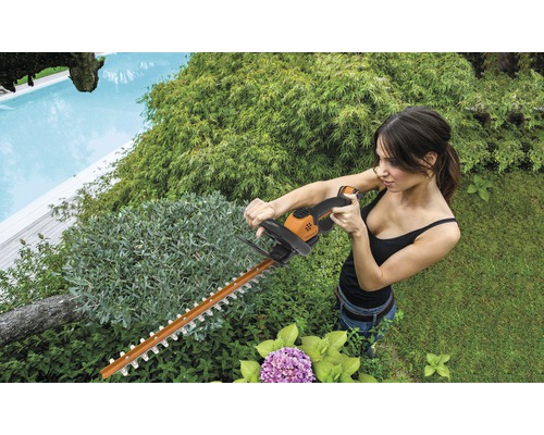 Une femme taille une haie avec un taille-haie dans le jardin.