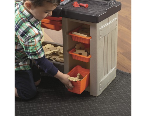 Kind spielt mit einer Werkbank mit Aufbewahrungsboxen und Holzspielzeug.