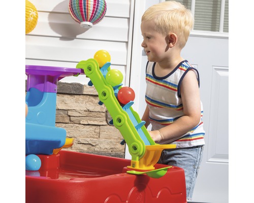Kind spielt mit einem bunten Wasserspieltisch mit Bällen im Garten.