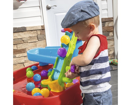 Kind spielt mit Wasser- und Balltisch im Freien