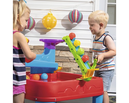 Zwei Kinder spielen mit einem bunten Step2 Murmel-Wasserspieltisch im Freien.