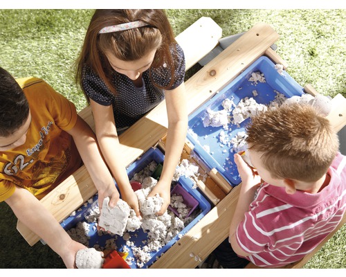 Drei Kinder spielen mit Sand an einem Sandtisch im Freien.