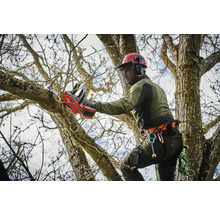 Un arboriste équipé d''un casque et de vêtements de protection coupe une branche avec une tronçonneuse à batterie.