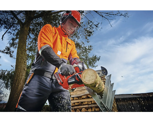 Une personne portant des vêtements de protection coupe un morceau de bois sur un chevalet de sciage avec une tronçonneuse à batterie.