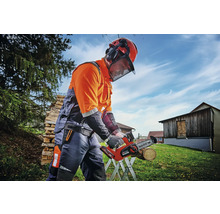 Personne portant un casque de protection et une protection auditive travaillant avec une tronçonneuse à batterie à l''extérieur.
