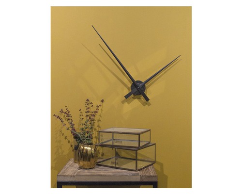 Scène décorative avec horloge murale, pot de fleurs doré et boîtes en verre sur une table.