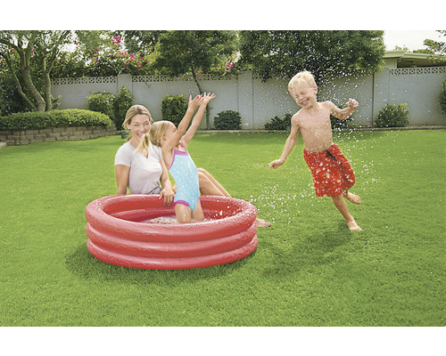 Mutter und Kinder spielen mit einem Planschbecken im Garten.