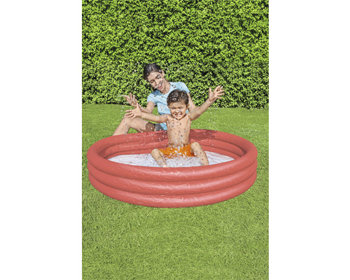 Mutter und Kind spielen in einem runden, roten Planschbecken im Garten.