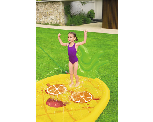 Mädchen spielt mit aufblasbarer Ananas-Wassersprinkler Matte im Garten.