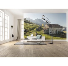 Wohnzimmer mit Fototapete eines Steinhauses in einer grünen Hügellandschaft