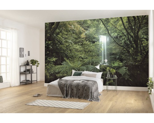 Helles Schlafzimmer mit Fototapete eines Waldes mit Wasserfall, Bett mit Decke und Nachttisch