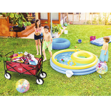 Szene im Garten mit Kindern, einem Bollerwagen mit Spielsachen und einem Planschbecken