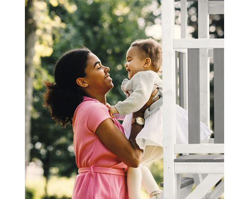 Eine Frau hält ein Kind in der Nähe eines Spielgerüsts im Freien.