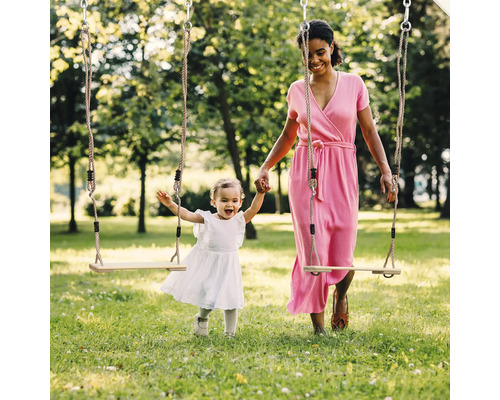 Mutter und Kind spielen mit einer Holzschaukel im Garten.