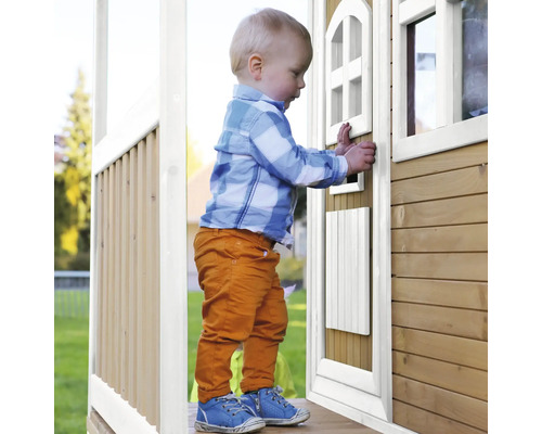 Jeune enfant debout devant une cabane de jeu en bois avec porte