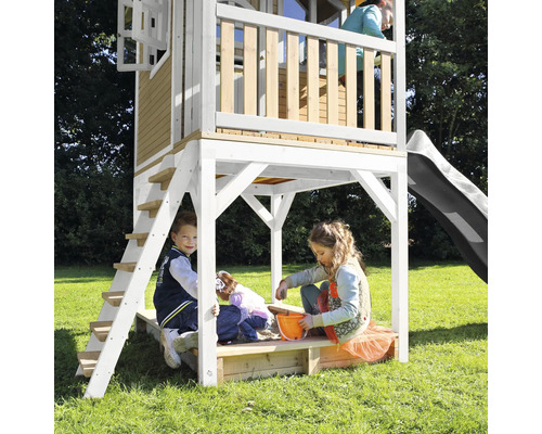 Maisonnette avec toboggan, échelle et bac à sable pour enfants dans le jardin.