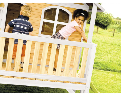 Kinder spielen in einem Holzspielhaus mit Rutsche im Garten.